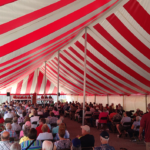 Many people sitting in a red and white striped tent