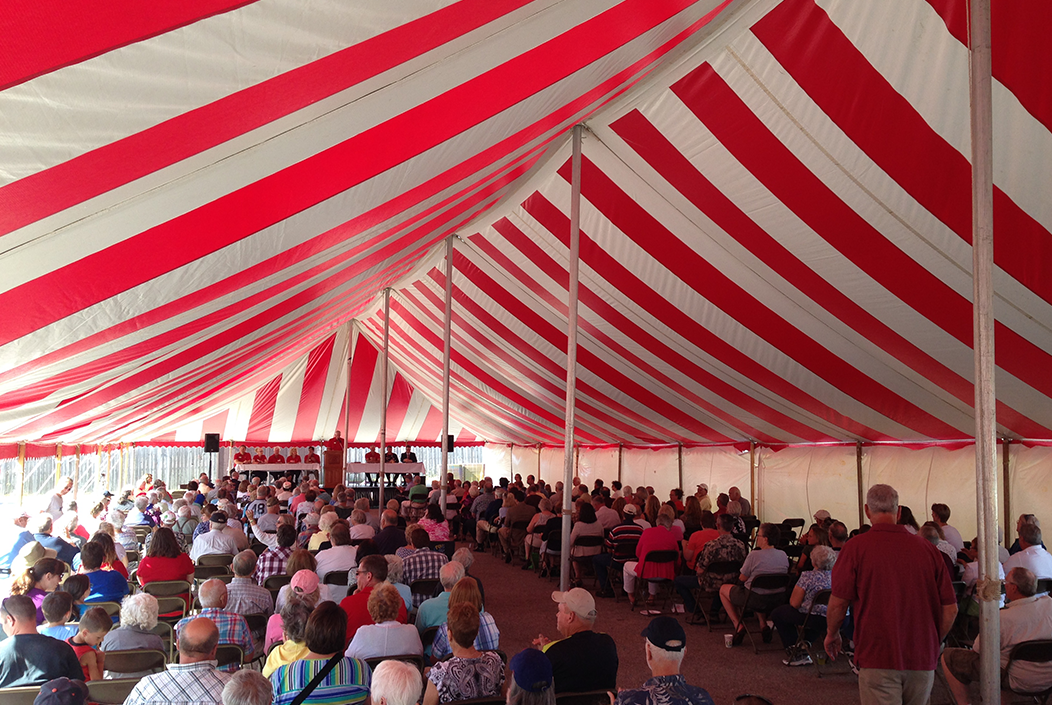 Many people sitting in a red and white striped tent