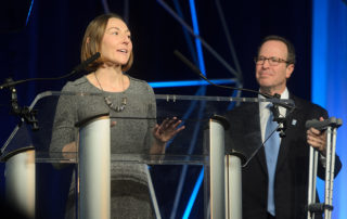 woman speaking at podium with man in background