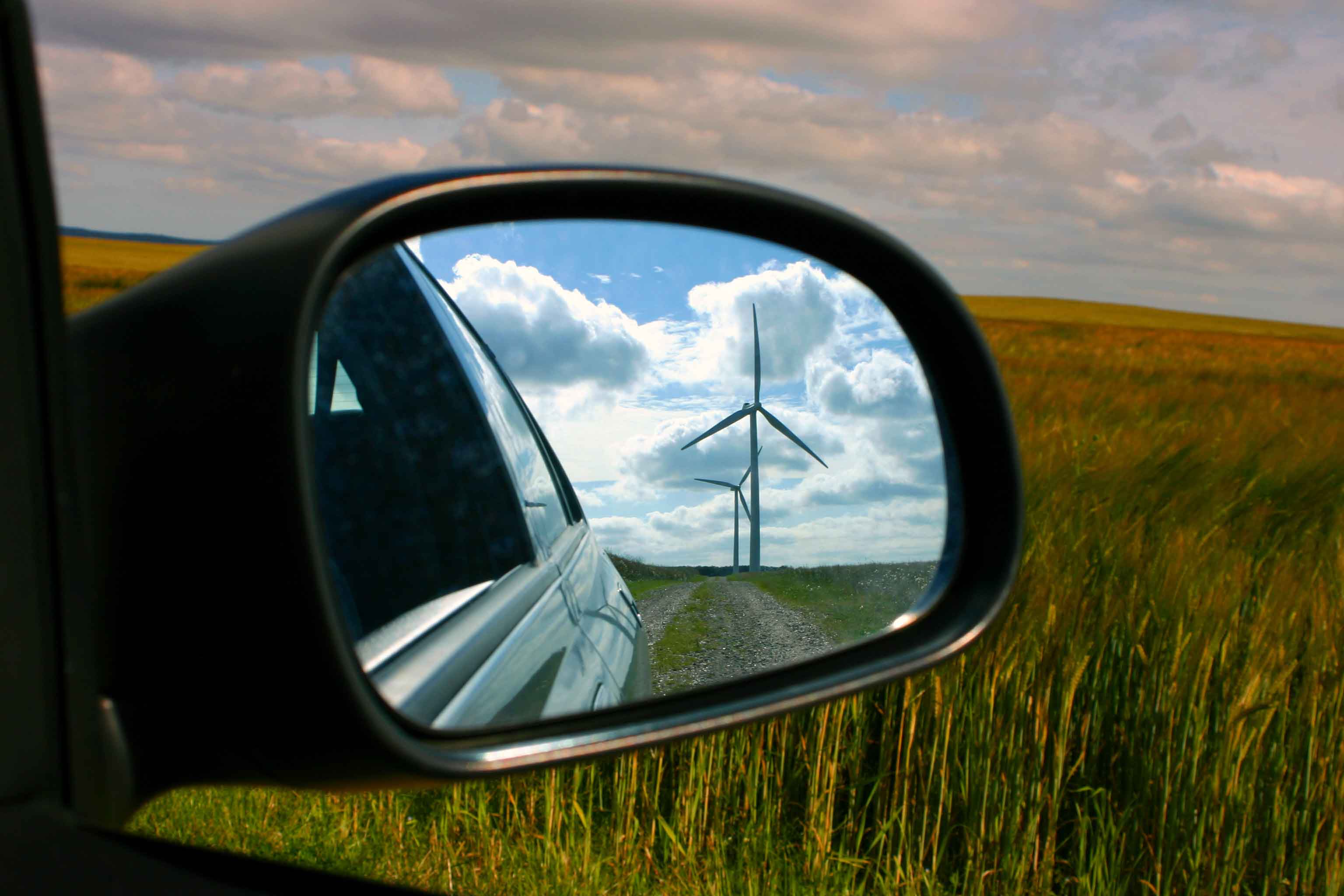 Side mirror of a car with a reflection of wind turbines